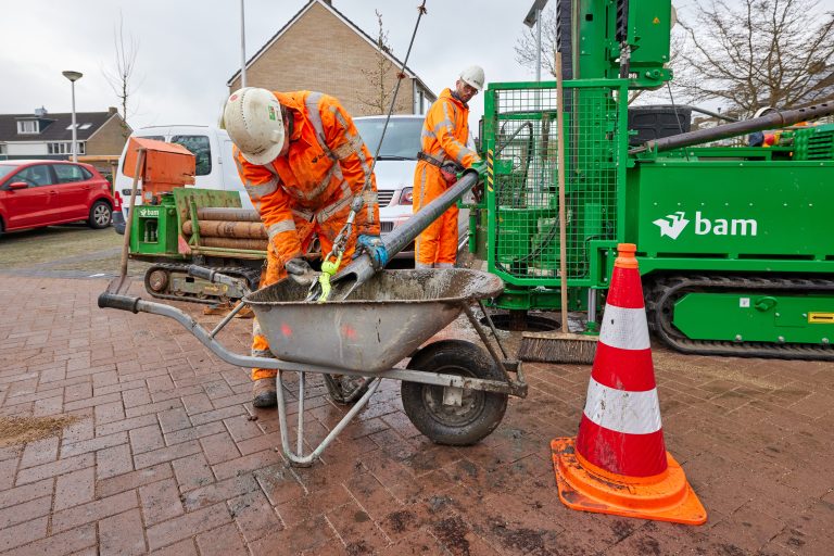 Afbeelding van werkende mannen in oranje outfit op straat.